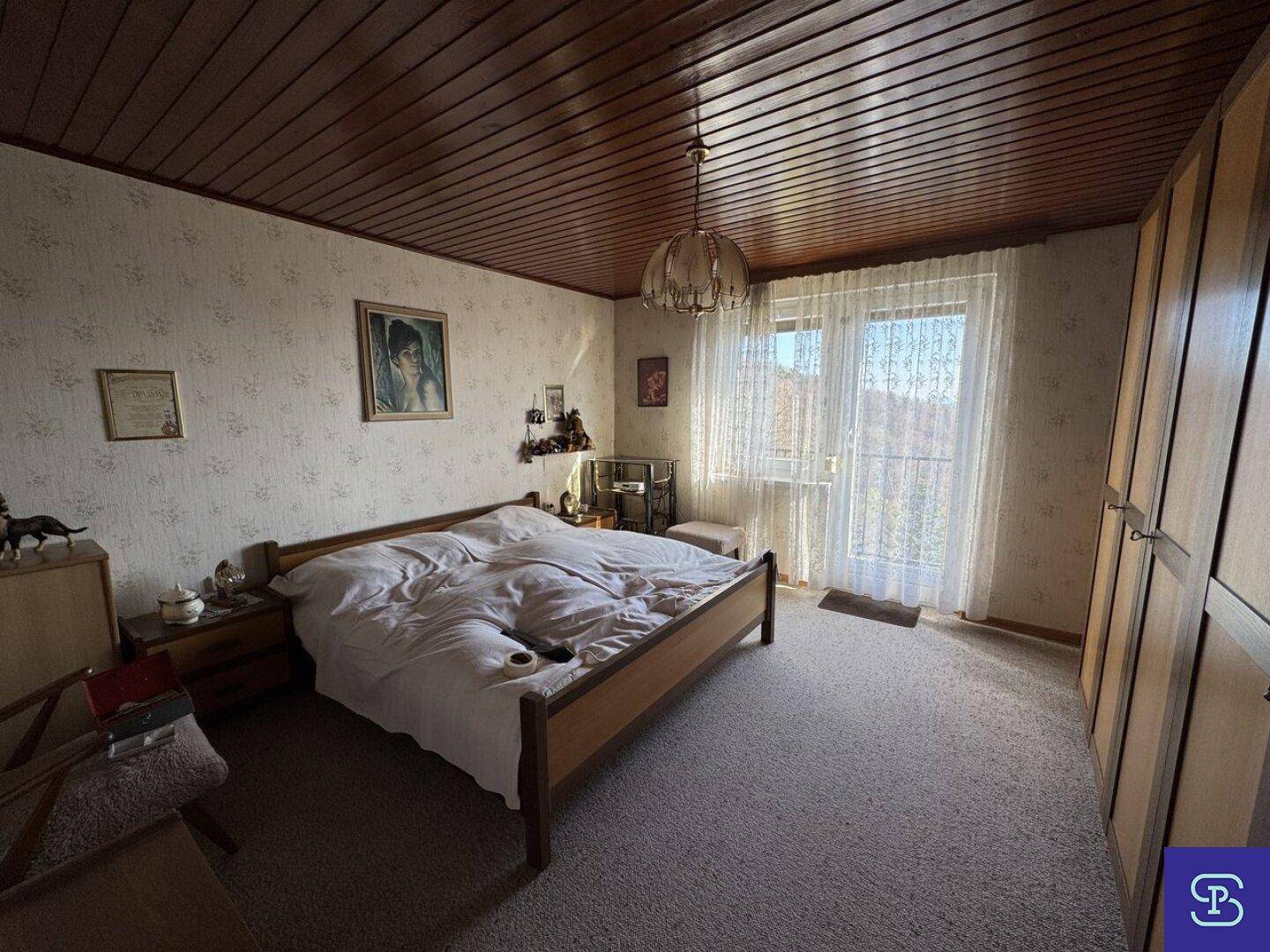 Geräumiges Schlafzimmer mit Holzbett, Teppichboden und Zugang zu einem Balkon.