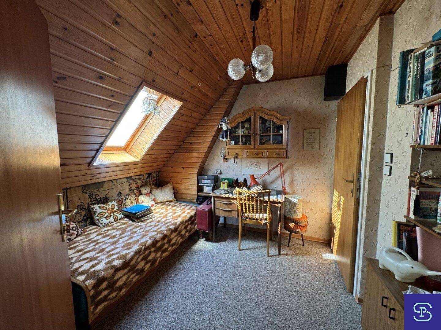 Gemütliches Schlafzimmer im Dachgeschoss mit Holzverkleidung, Dachfenster und integriertem Arbeitsbereich.