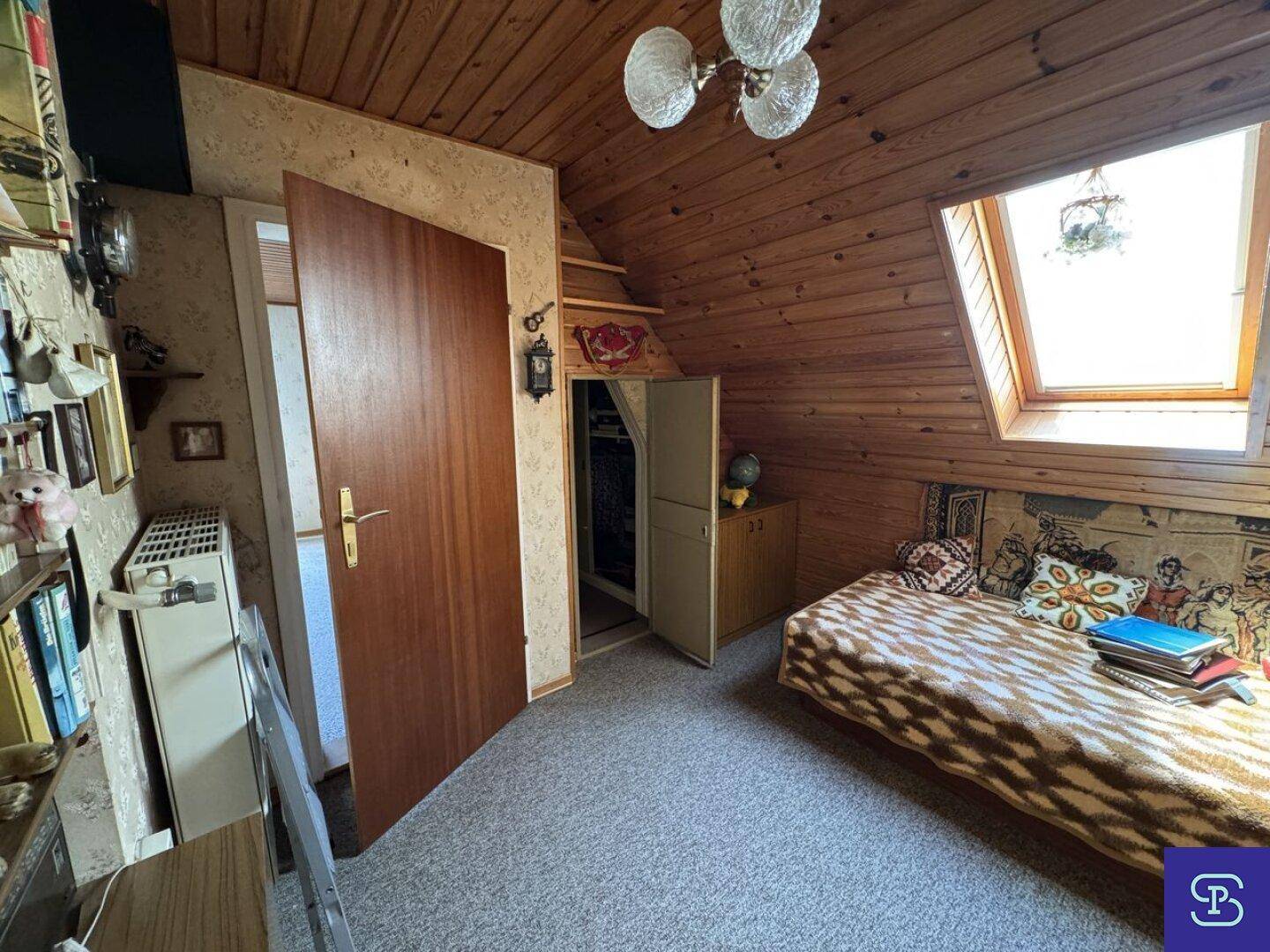 Helles Dachgeschosszimmer mit Holzdecke, Teppichboden und praktischem Stauraum.