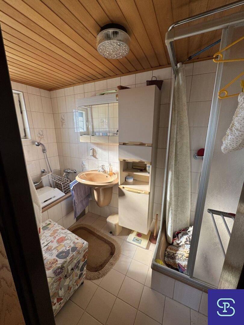 Badezimmer mit Duschkabine, Waschbecken und Holzdecke in hellem Design.