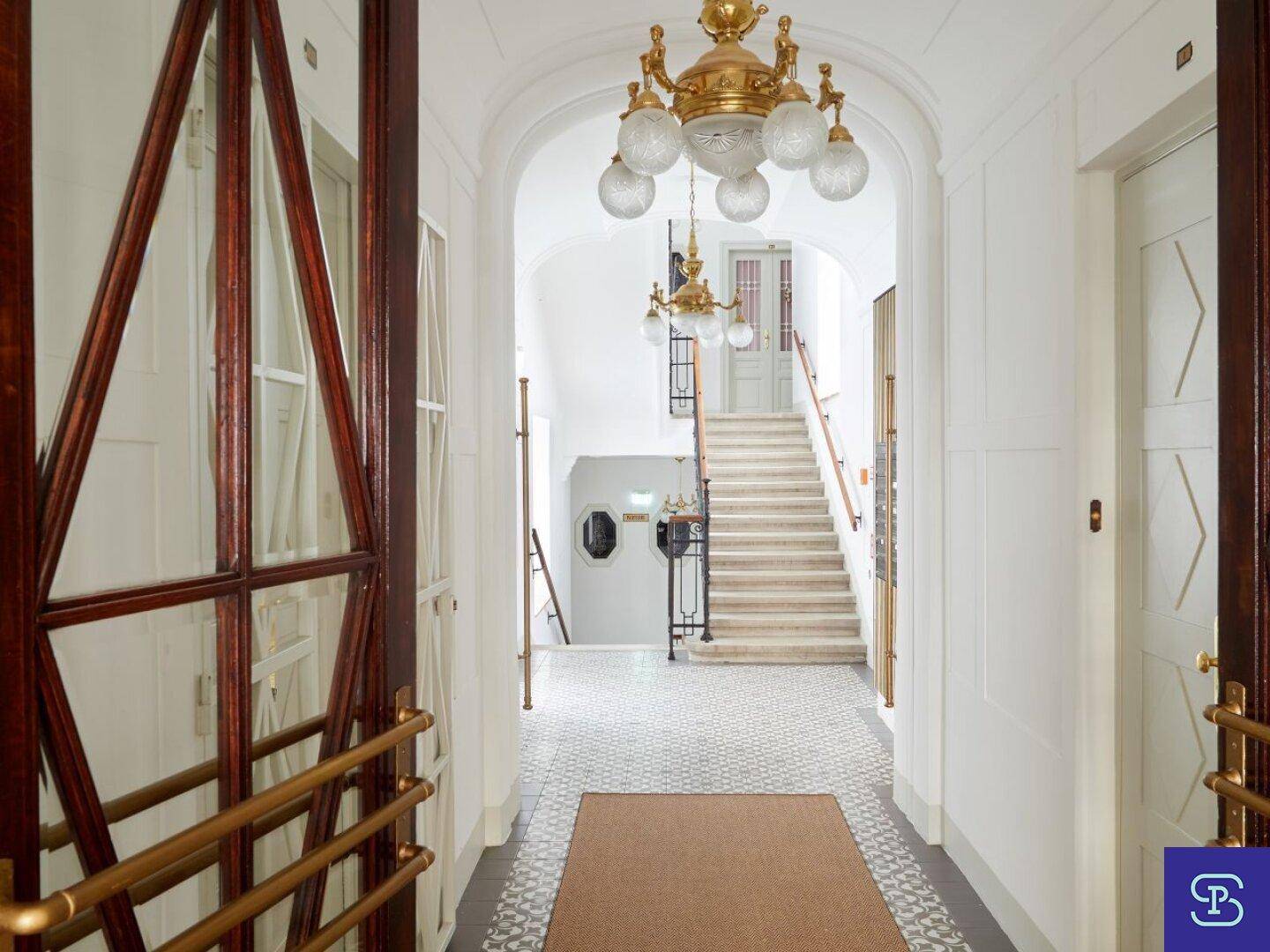 Heller Eingangsbereich mit gemustertem Boden, elegantem Kronleuchter und Zugang zum Treppenhaus.