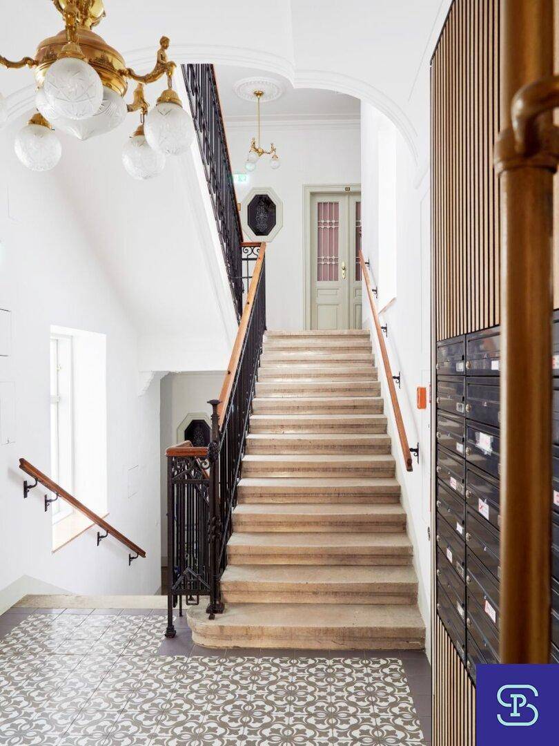 Elegantes Treppenhaus mit historischen Elementen, gemusterten Fliesen und prunkvollem Kronleuchter.