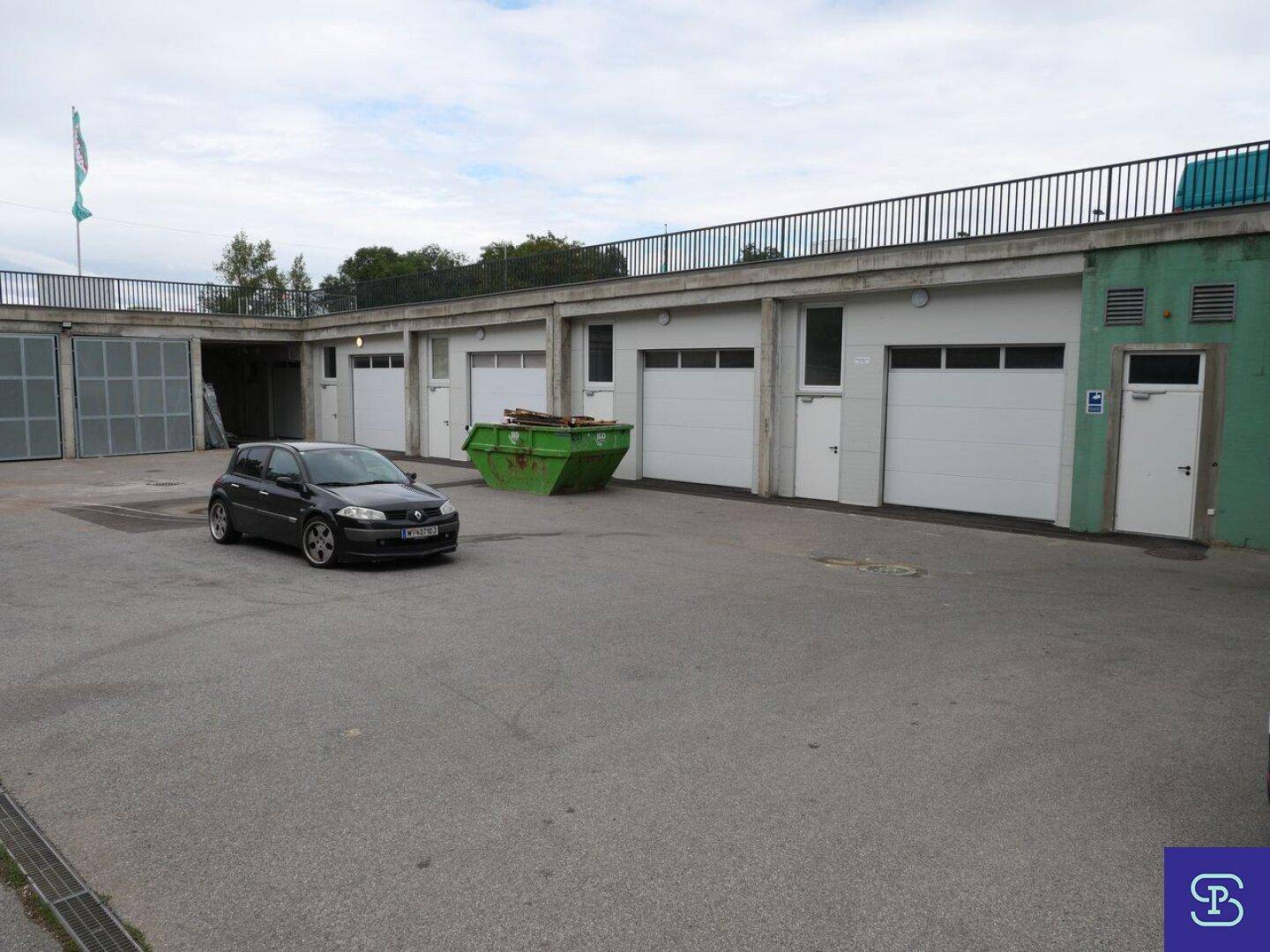 Außenansicht eines Gebäudes mit mehreren Garagentoren und einem großen asphaltierten Parkplatz.