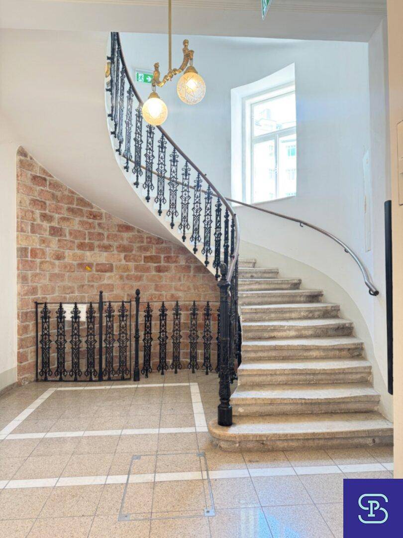 Elegante geschwungene Steintreppe mit schmiedeeisernem Geländer und freigelegter Ziegelwand im Eingangsbereich.