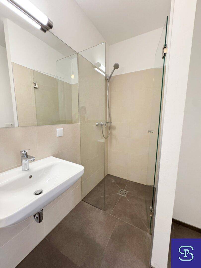 Modernes Badezimmer mit ebenerdiger Dusche, großem Spiegel und hellen Fliesen.