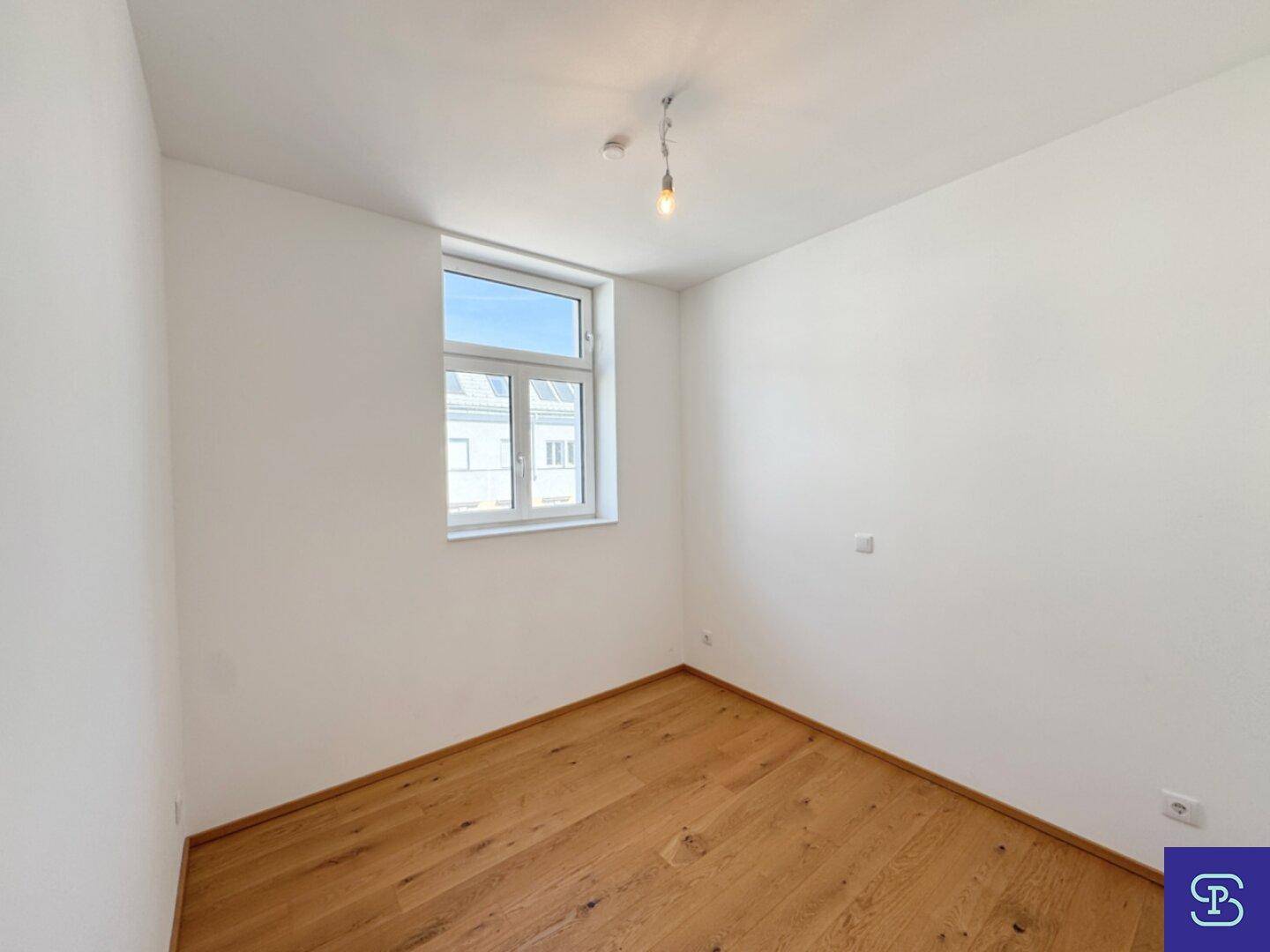 Ruhiges Schlafzimmer mit großem Fenster, Parkettboden und viel Tageslicht.