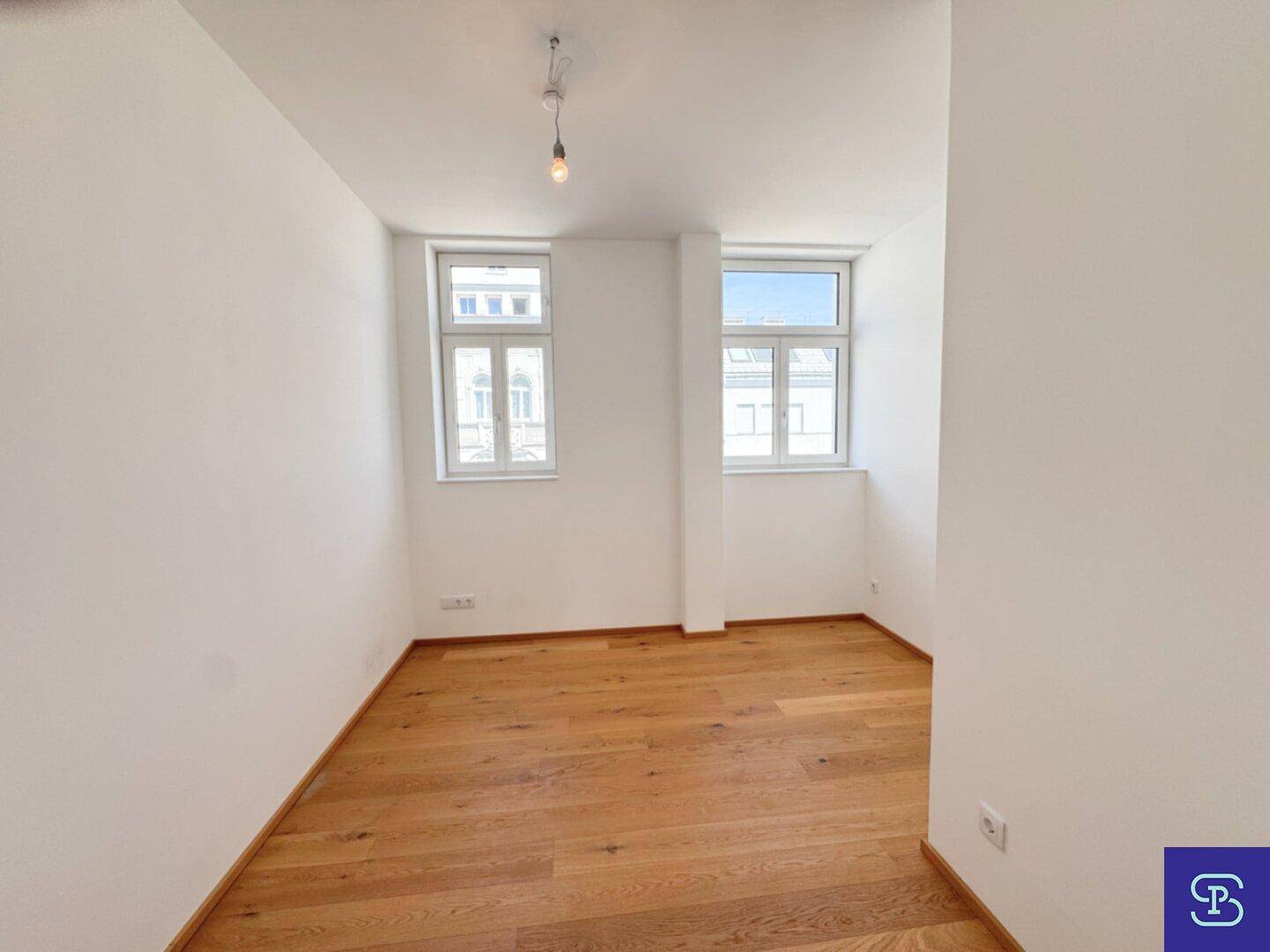 Geräumiges Schlafzimmer mit zwei Fenstern, Parkettboden und hellen Wänden.