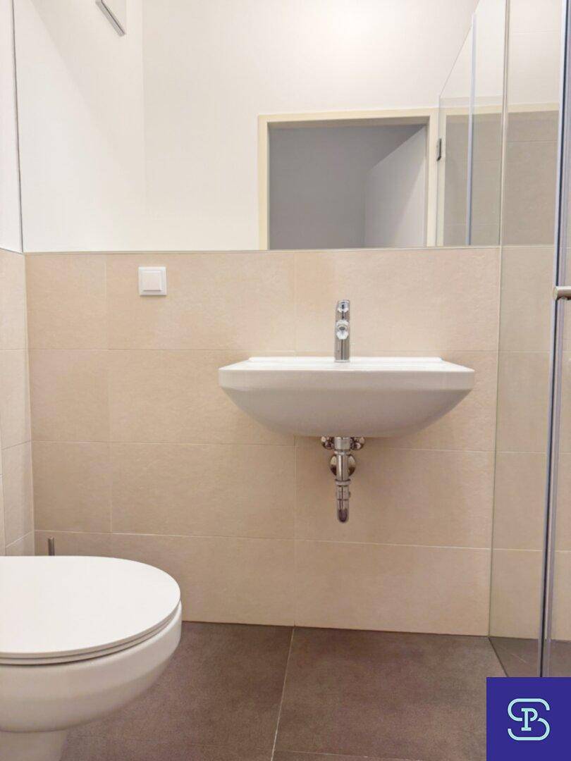Modernes Badezimmer mit Waschbecken, Toilette und hellen Fliesen, ausgestattet mit einem großen Spiegel.