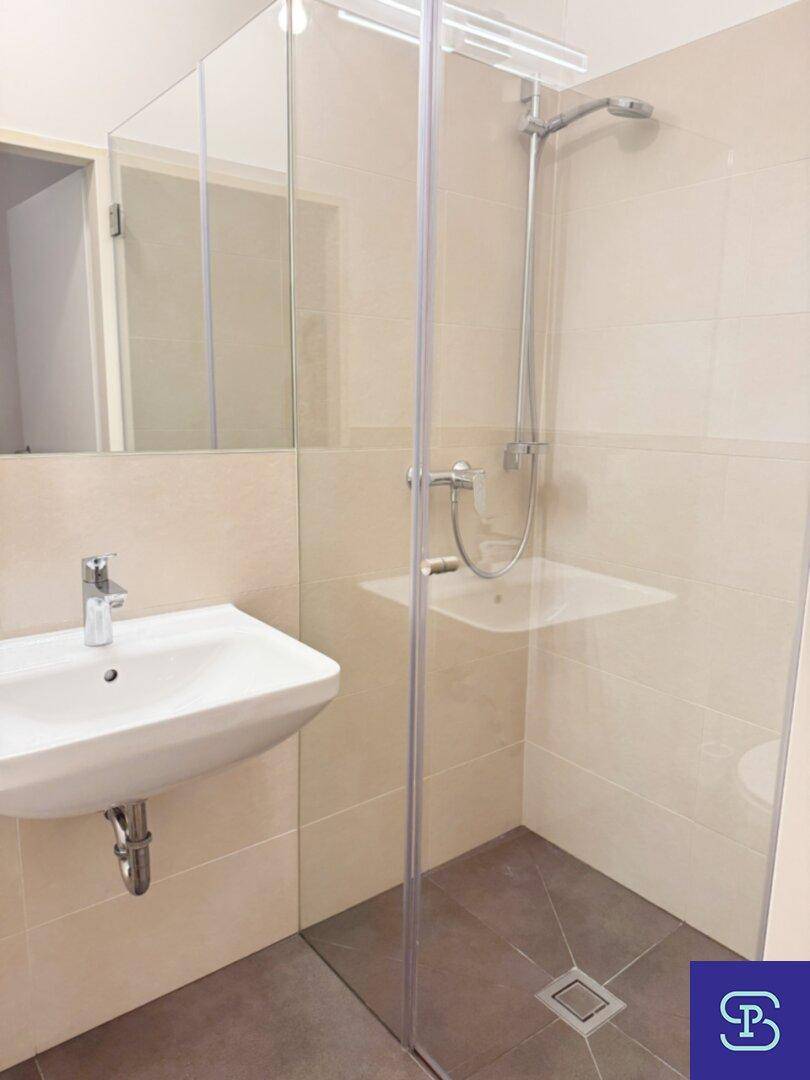 Modernes Badezimmer mit ebenerdiger Dusche, Waschbecken und hellen Fliesen, durch eine Glaswand abgetrennt.