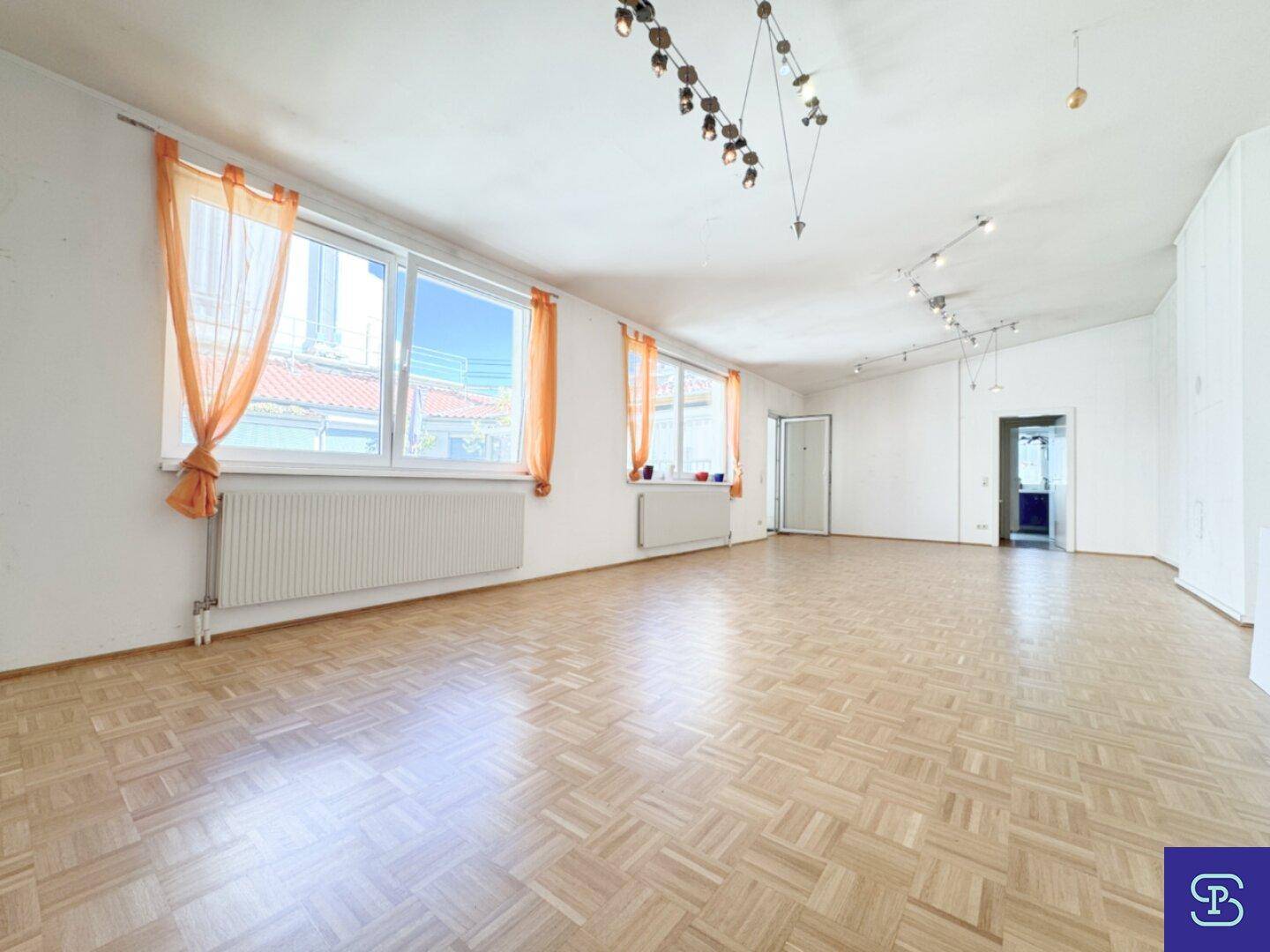 Geräumiges Wohnzimmer mit hellem Parkettboden, großen Fenstern und viel Tageslicht.