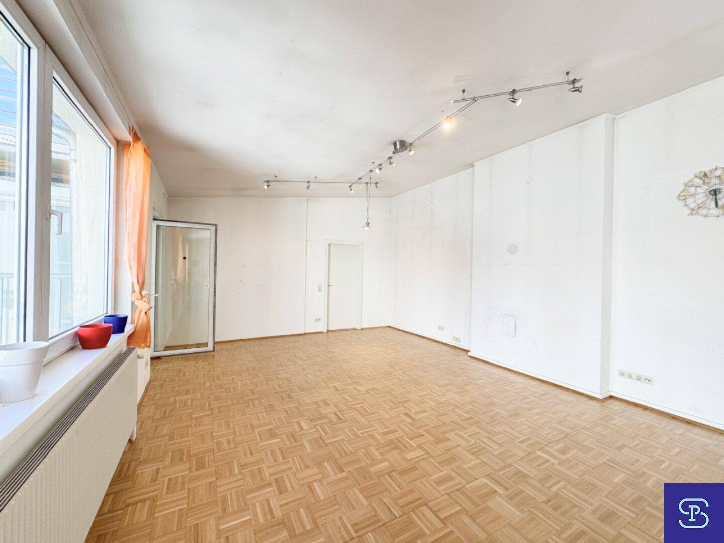 Weitläufiges Wohnzimmer mit Parkettboden und großen Fenstern, die viel Licht hereinlassen.