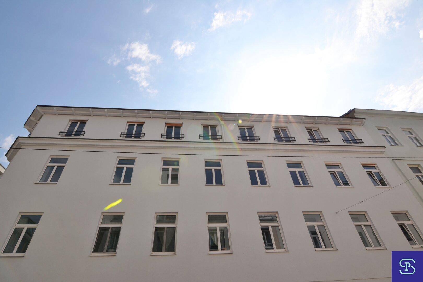Obere Etagen eines weißen Gebäudes mit vielen Fenstern unter blauem Himmel.