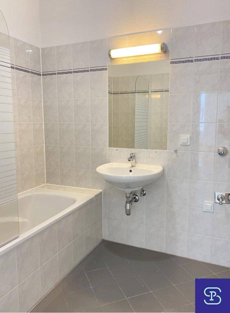 Helles Badezimmer mit Badewanne, Duschwand, Waschbecken und Wandspiegel.
