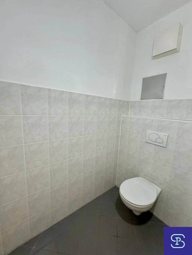 Separates WC mit wandhängender Toilette und hellgrauen Fliesen an den Wänden.