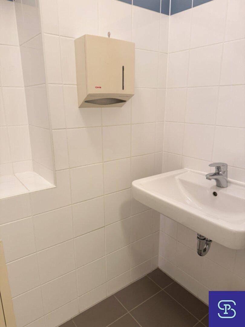 Toilettenraum mit Waschbecken, weißen Fliesen und einem Spender für Papierhandtücher.