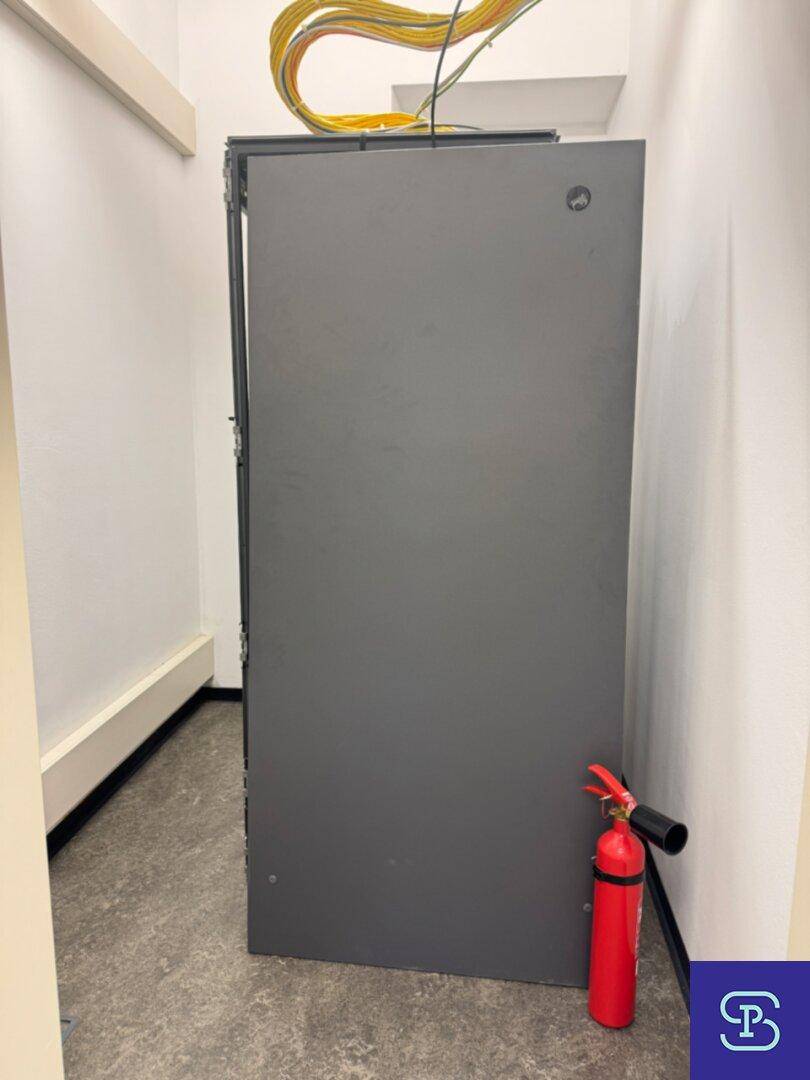 Serverraum mit einem großen Serverschrank und einem Feuerlöscher für die Sicherheit.