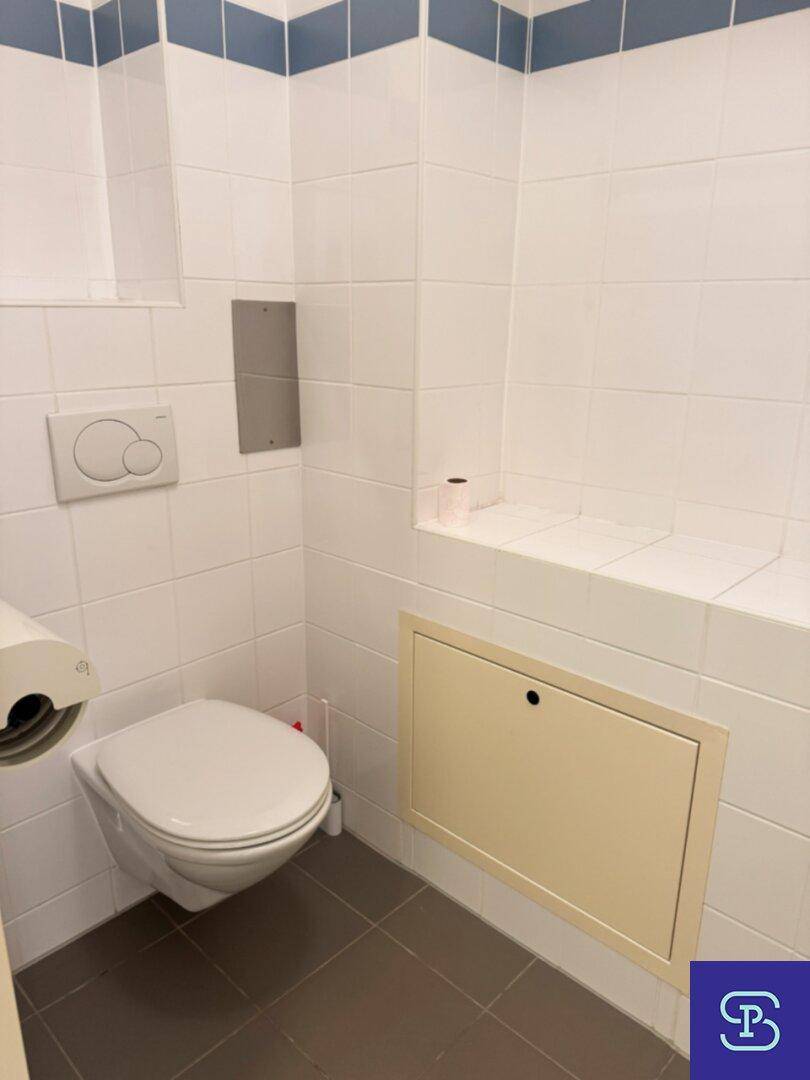 Saubere Toilette mit Wand-WC, weißen Fliesen und einem kleinen Ablagebereich.