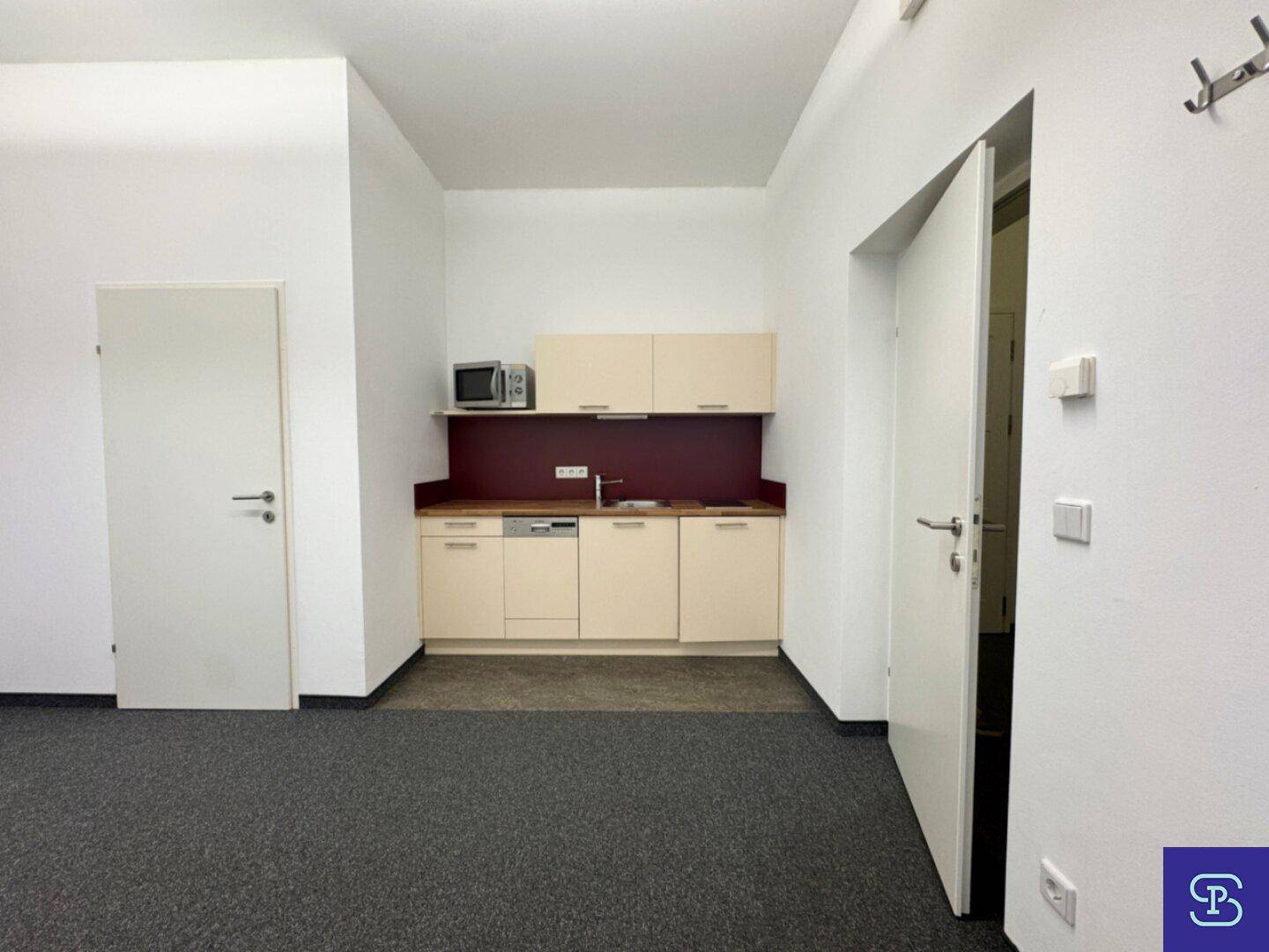 Funktionale Küchenzeile mit beigen Schränken, Spülmaschine und Mikrowelle in einem Bürobereich.