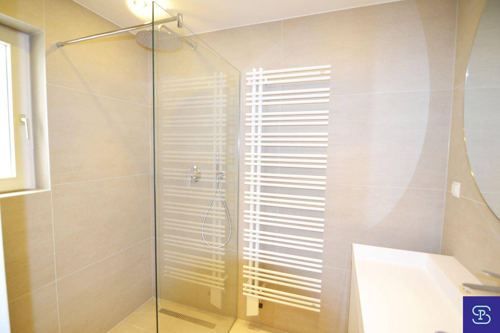 Modernes Badezimmer mit großen beigefarbenen Fliesen, ebenerdiger Dusche und praktischem Handtuchheizkörper.