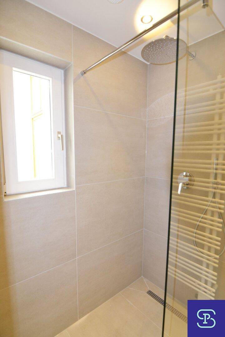 Ebenerdige Dusche mit Regenduschkopf, Glasabtrennung und Fenster im hellen, modernen Badezimmer.
