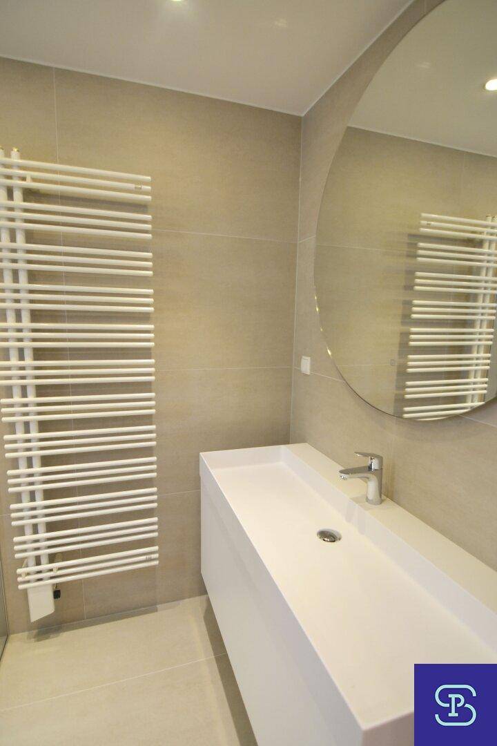 Moderner Waschtisch mit Einzelwaschbecken, rundem Spiegel und praktischem Handtuchheizkörper im Badezimmer.