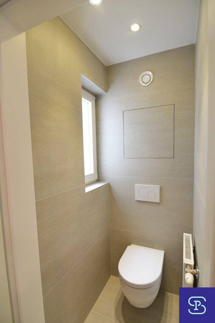 Separates Gäste-WC mit wandhängender Toilette, Fenster und beigefarbenen Fliesen, hell und funktional.