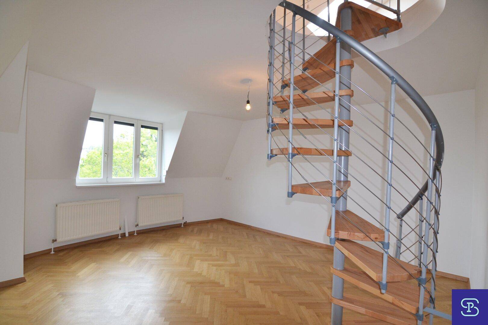 Helles Dachgeschosszimmer mit Fischgrätparkett, Fenster, Heizkörpern und eleganter Wendeltreppe nach oben.