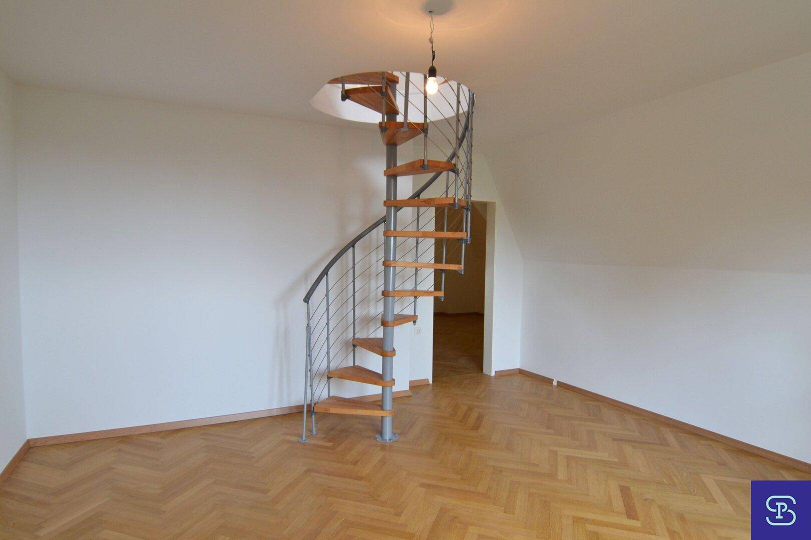 Geräumiges Dachgeschosszimmer mit Fischgrätparkett und eleganter Wendeltreppe, die nach unten führt.