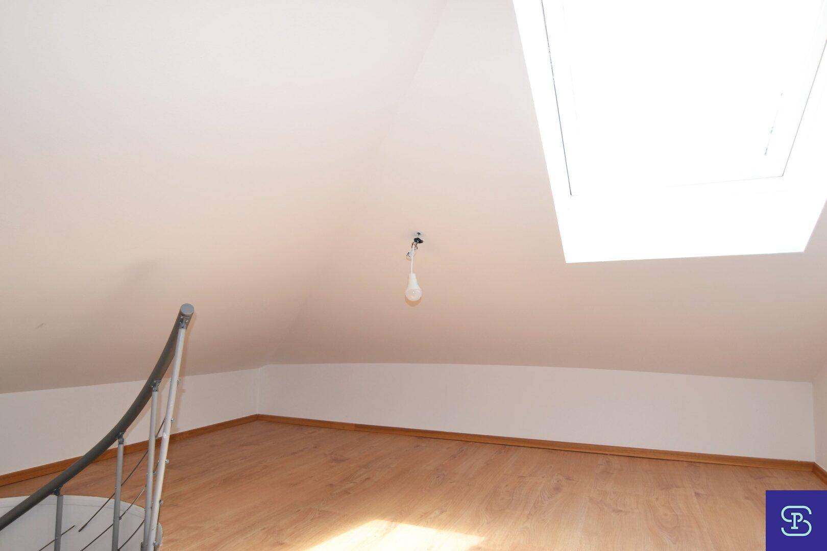 Helles Dachgeschosszimmer mit Laminatboden, großem Dachfenster und schrägen Wänden, viel Tageslicht.