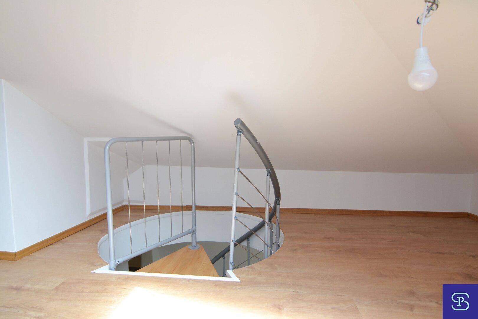 Dachgeschosszimmer mit Laminatboden und Zugang zur Wendeltreppe, die in die untere Etage führt.