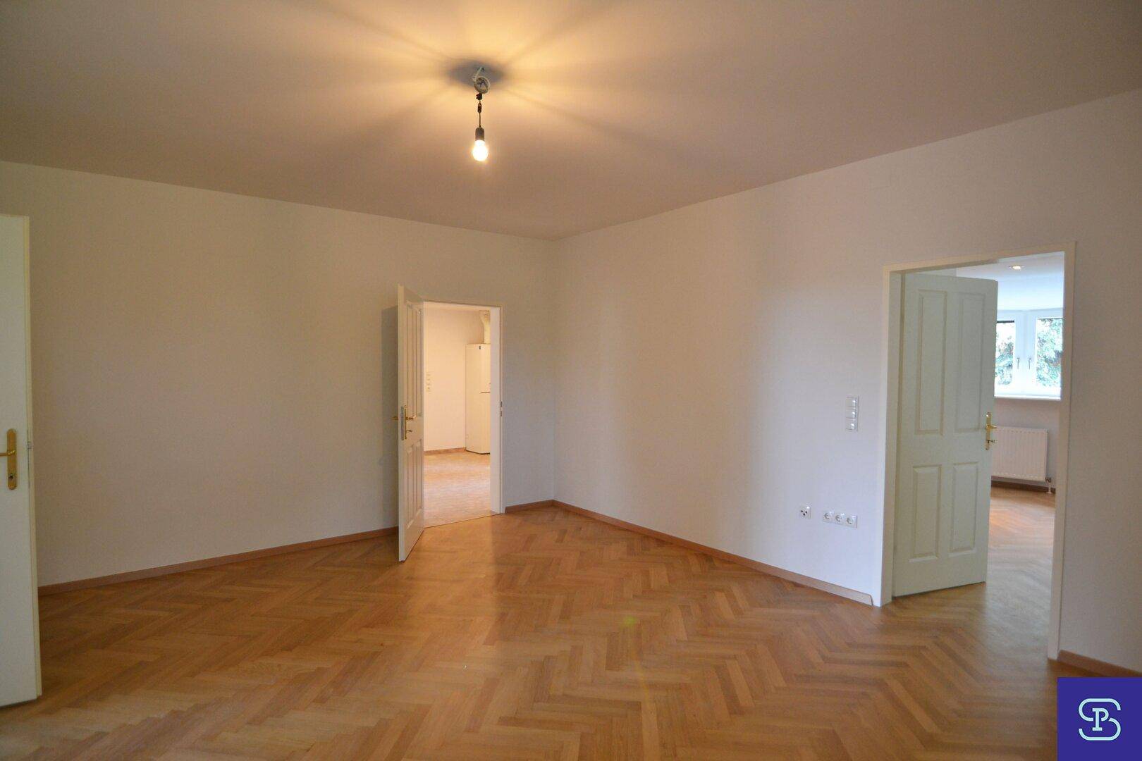 Geräumiges Zimmer mit Fischgrätparkett und Zugang zu mehreren angrenzenden Räumen, vielseitig nutzbar.