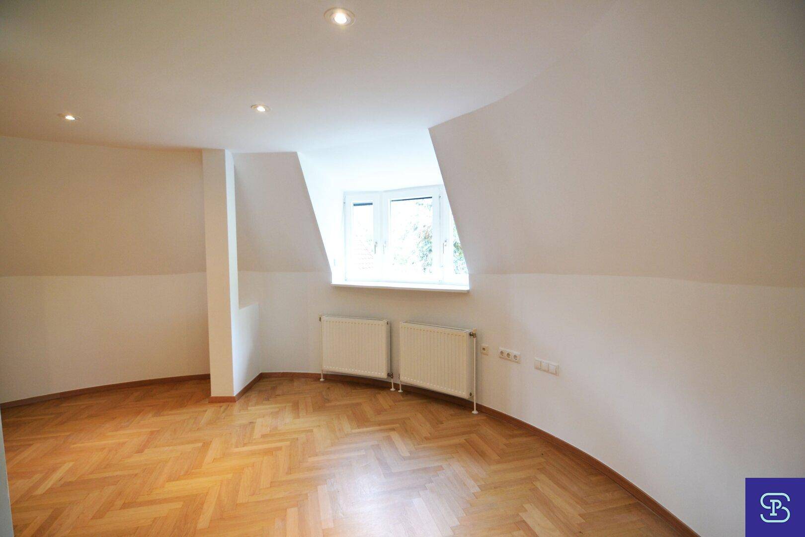 Helles Dachgeschosszimmer mit Fischgrätparkett, Fenster, zwei Heizkörpern und modernen Einbaustrahlern.