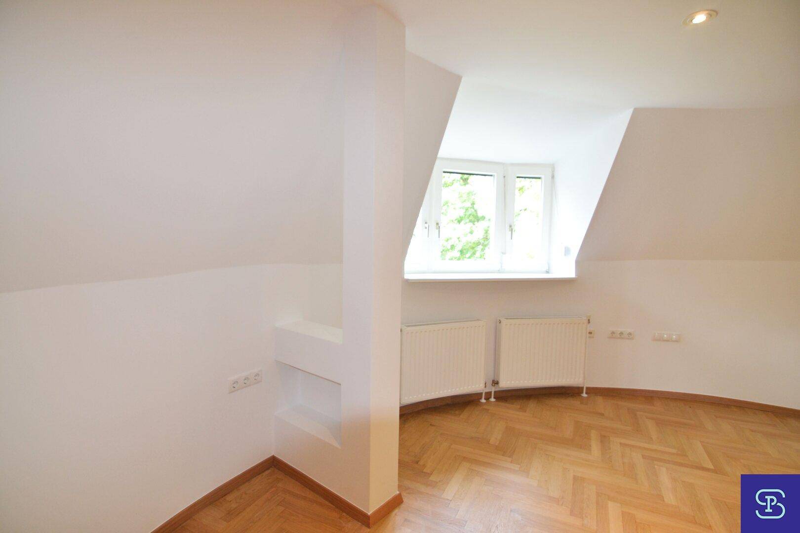 Helles Dachgeschosszimmer mit Fischgrätparkett, Fenster, Heizkörpern und praktischer integrierter Nische.