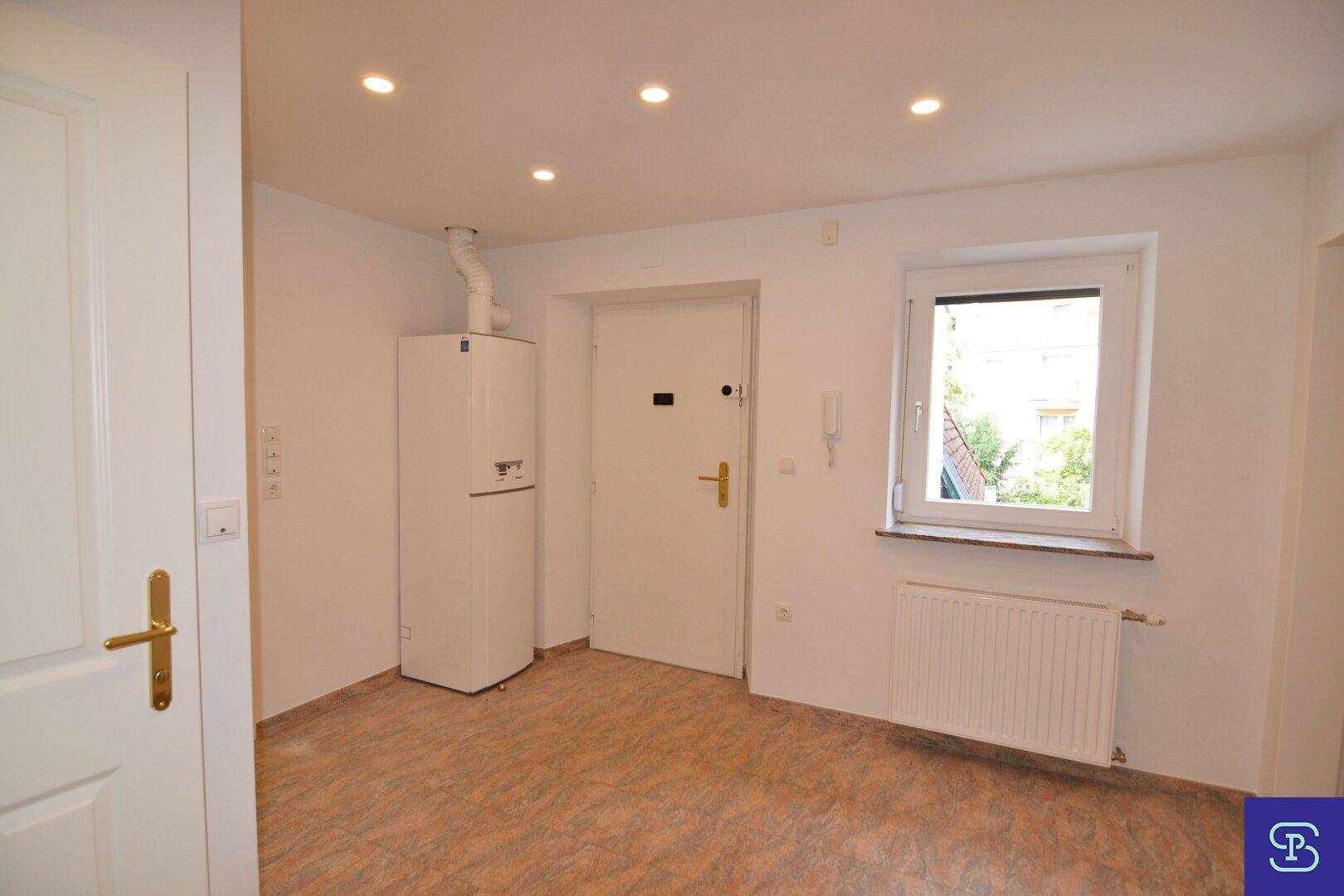 Heller Eingangsbereich mit Fliesenboden, Fenster, Heizkörper und sichtbarer Heizungsanlage.