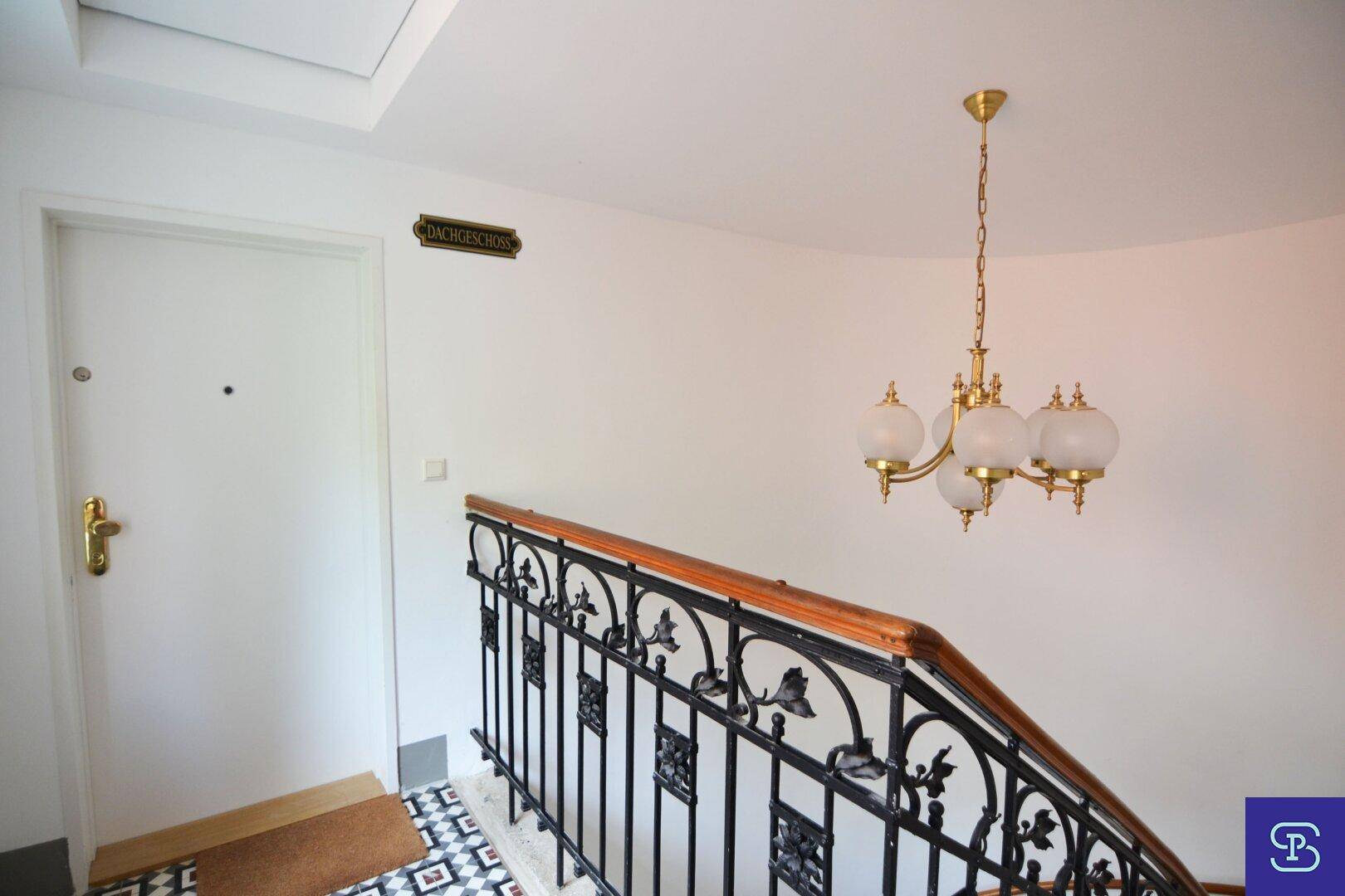 Historisches Treppenhaus mit schmiedeeisernem Geländer, elegantem Kronleuchter und Zugang zum Dachgeschoss.