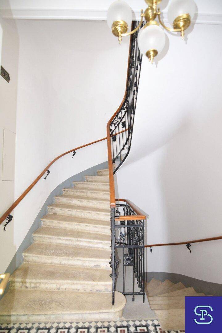 Elegantes Treppenhaus mit geschwungener Steintreppe, schmiedeeisernem Geländer und klassischem Kronleuchter.