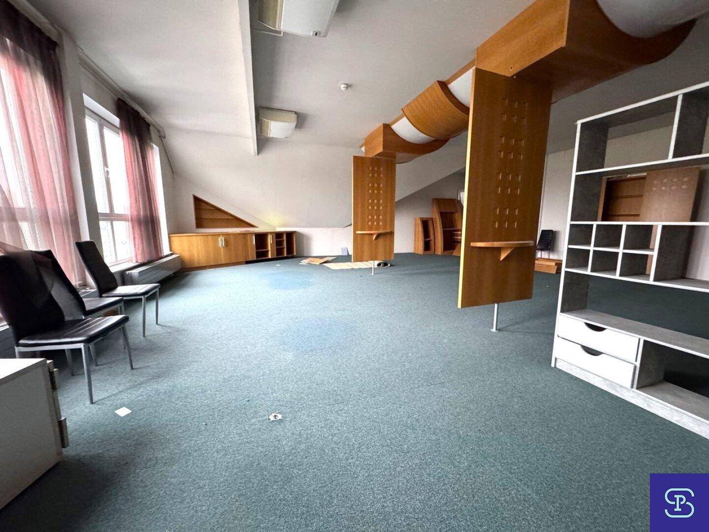 Heller Büroraum im Dachgeschoss mit großen Fenstern, grünem Teppich und Holzvertäfelungen.