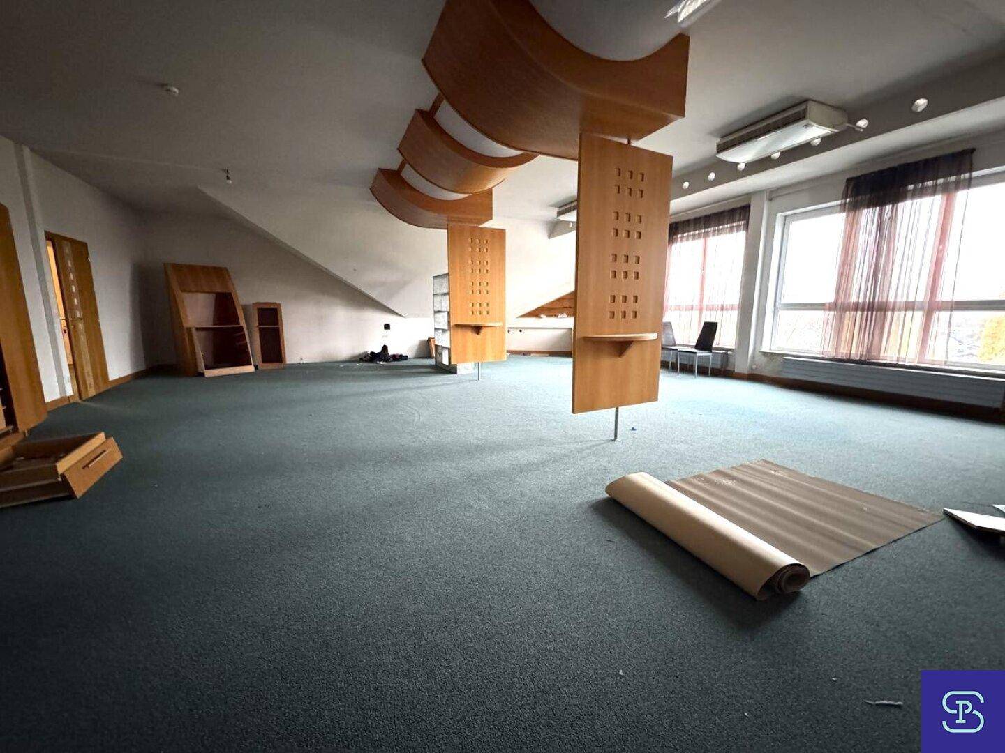 Großer Bürobereich mit Teppichboden, Dachschrägen und Fenstern, der eine Renovierung benötigt.