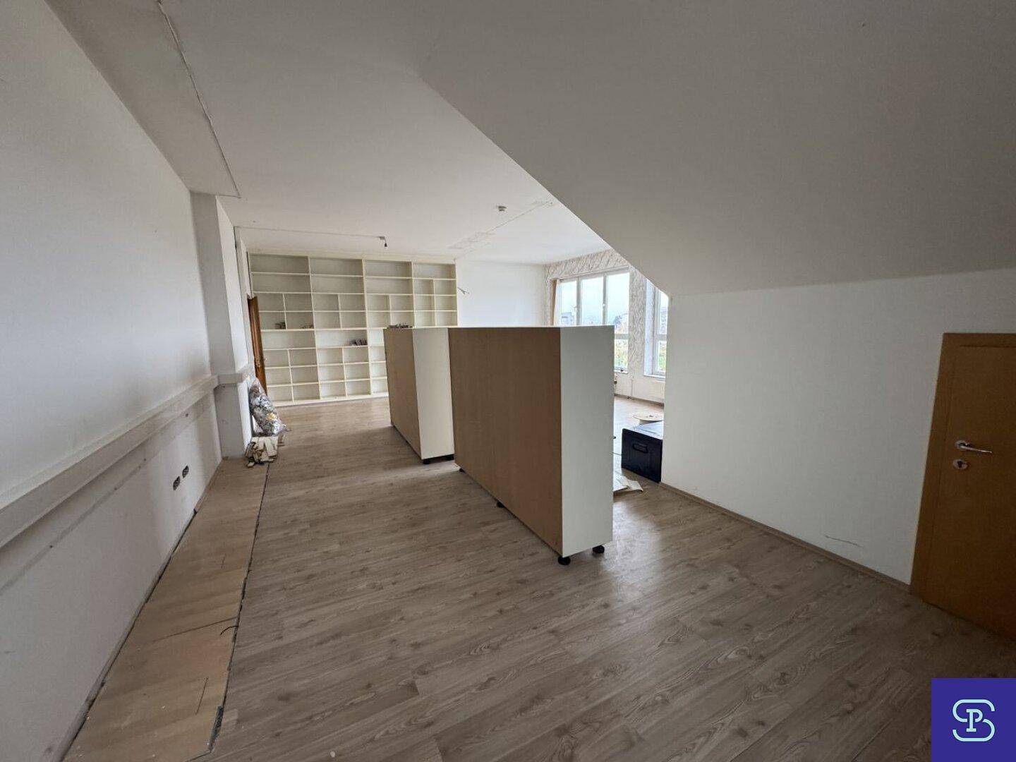 Langer Innenraum mit Laminatboden, eingebauten Regalen und schräger Decke, der auf eine Neugestaltung wartet.