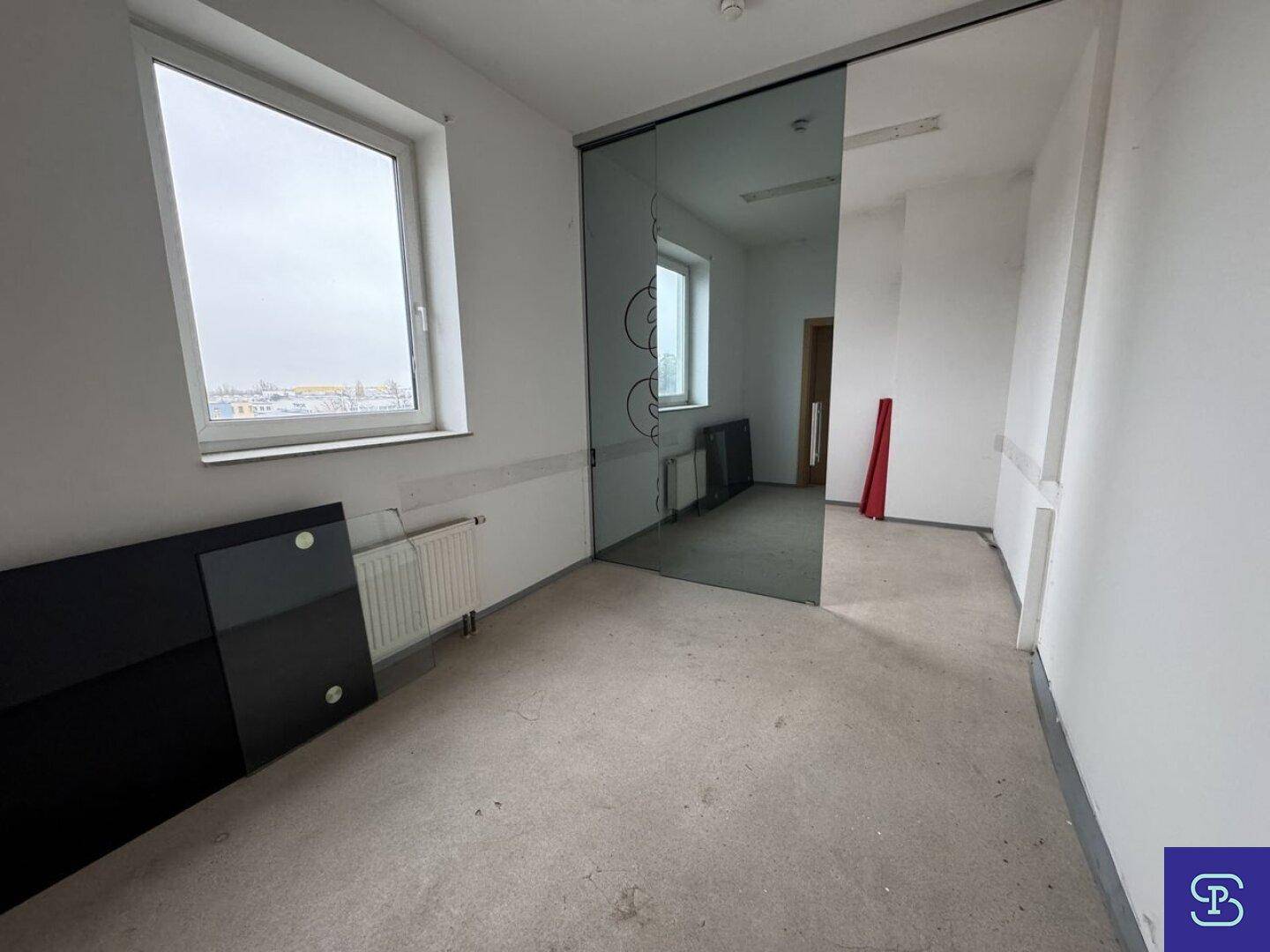 Kleinerer Raum mit Teppichboden, Fenster und einer modernen Glasschiebetür, der Renovierungsbedarf aufweist.