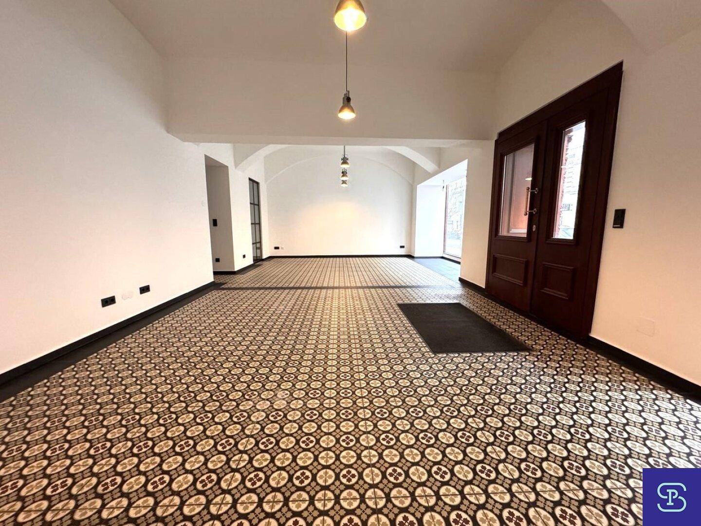 Eingangsbereich eines Gewerberaums mit hohen Decken, Holztüren und dekorativen Bodenfliesen.