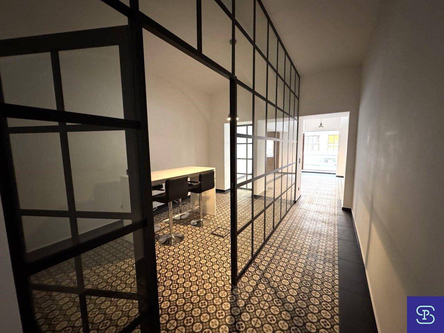 Moderner Bürobereich mit Glas-Stahl-Trennwänden und gemustertem Fliesenboden.