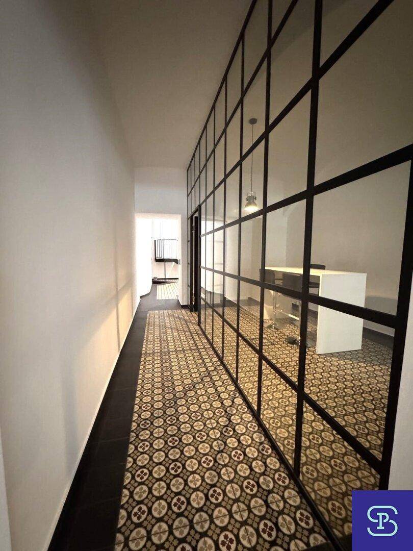 Langer Flur mit Glas-Stahl-Trennwänden und gemustertem Fliesenboden, der zu weiteren Räumen führt.