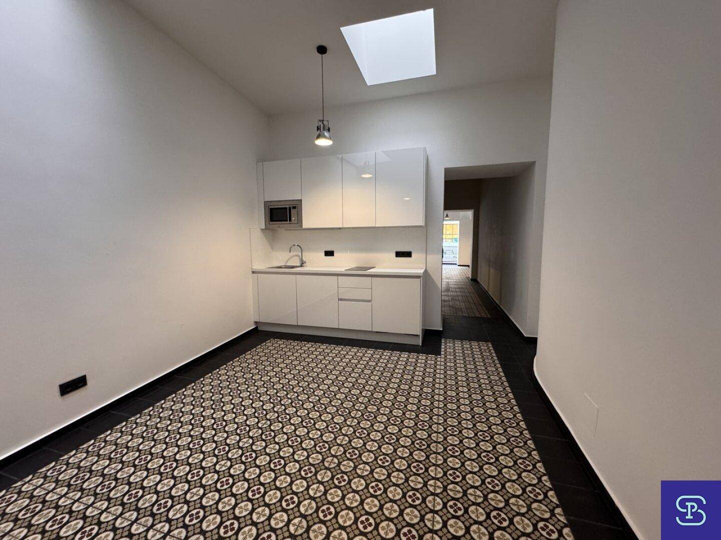 Kleine, moderne Küchenzeile mit weißen Hochglanzschränken und Oberlicht für natürliches Licht.