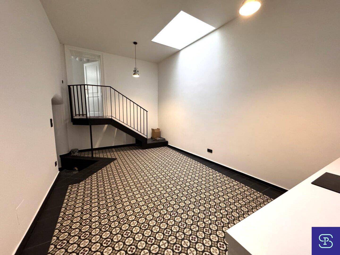 Heller Raum mit einer modernen Treppe, Oberlicht und gemustertem Fliesenboden.