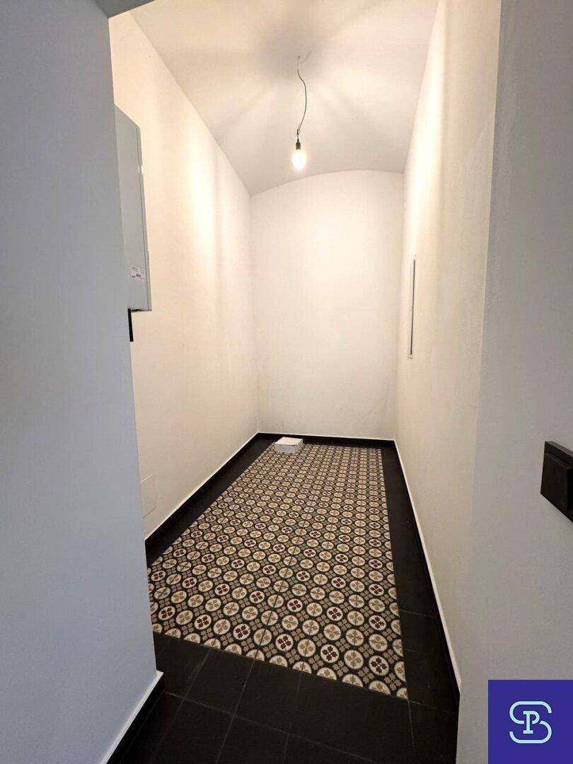 Schmaler Flur mit gemustertem Fliesenboden und weißen Wänden, einfach beleuchtet.