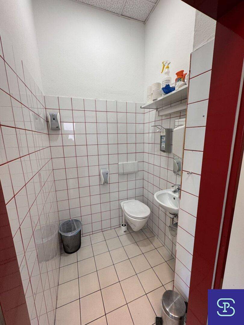 Funktionale Toilette mit Waschbecken und Fliesen, gut gepflegt und mit grundlegender Ausstattung für Besucher und Personal.