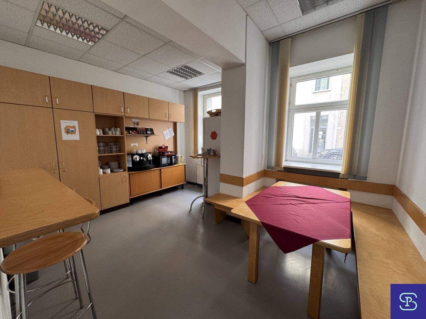 Pausenraum mit Holzbänken, Tischen und einer Küchenzeile, ideal für Mitarbeiter.