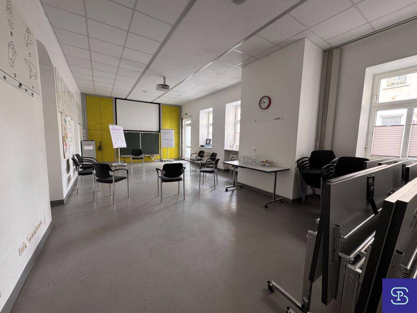 Großer Konferenzraum mit hellem Boden, Projektor und vielen Stühlen, ideal für Präsentationen.