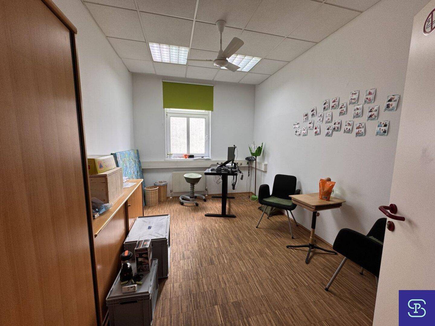 Büro mit Holzparkett, Deckenventilator und einem Arbeitsplatz, ergänzt durch einen Schrank und ein Fenster.